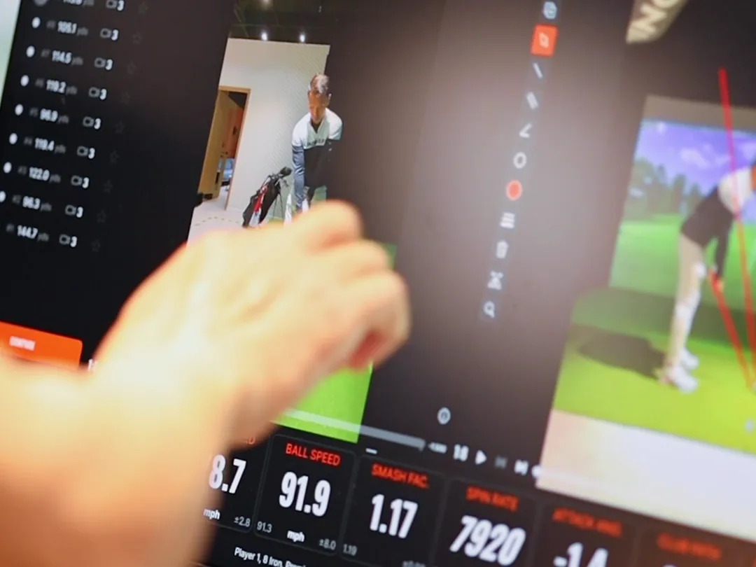A hand pointing to a golfer’s swing on a video replay screen